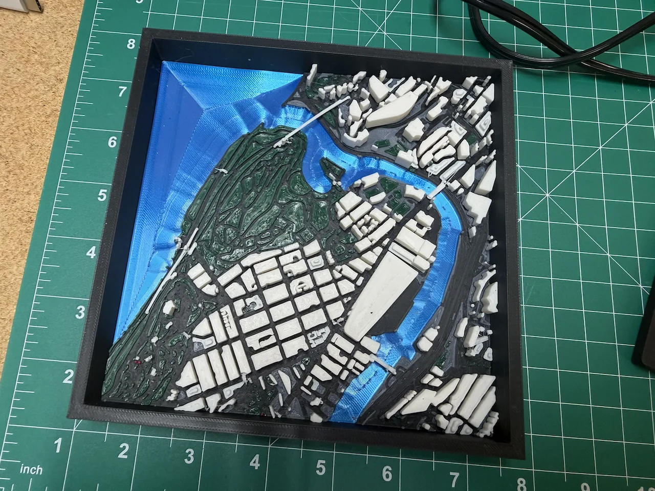 3D-printed multi-colour city model with terrain and water in a black frame
